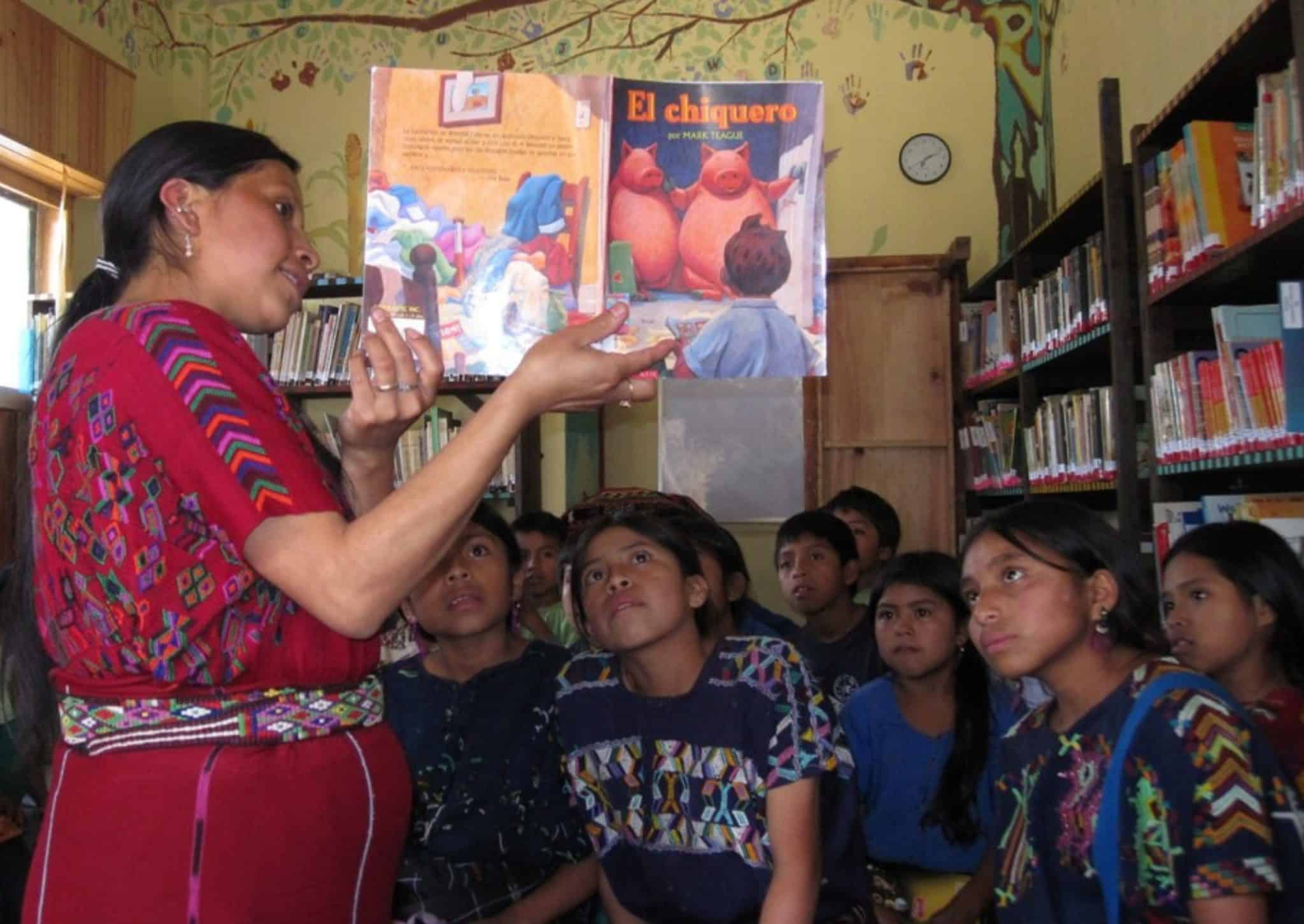 Woman reading "El chiguero" book to children in a library setting.