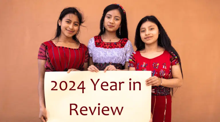Three Ixil girls holding a sign for 2024 Year in Review, celebrating education and community impact.