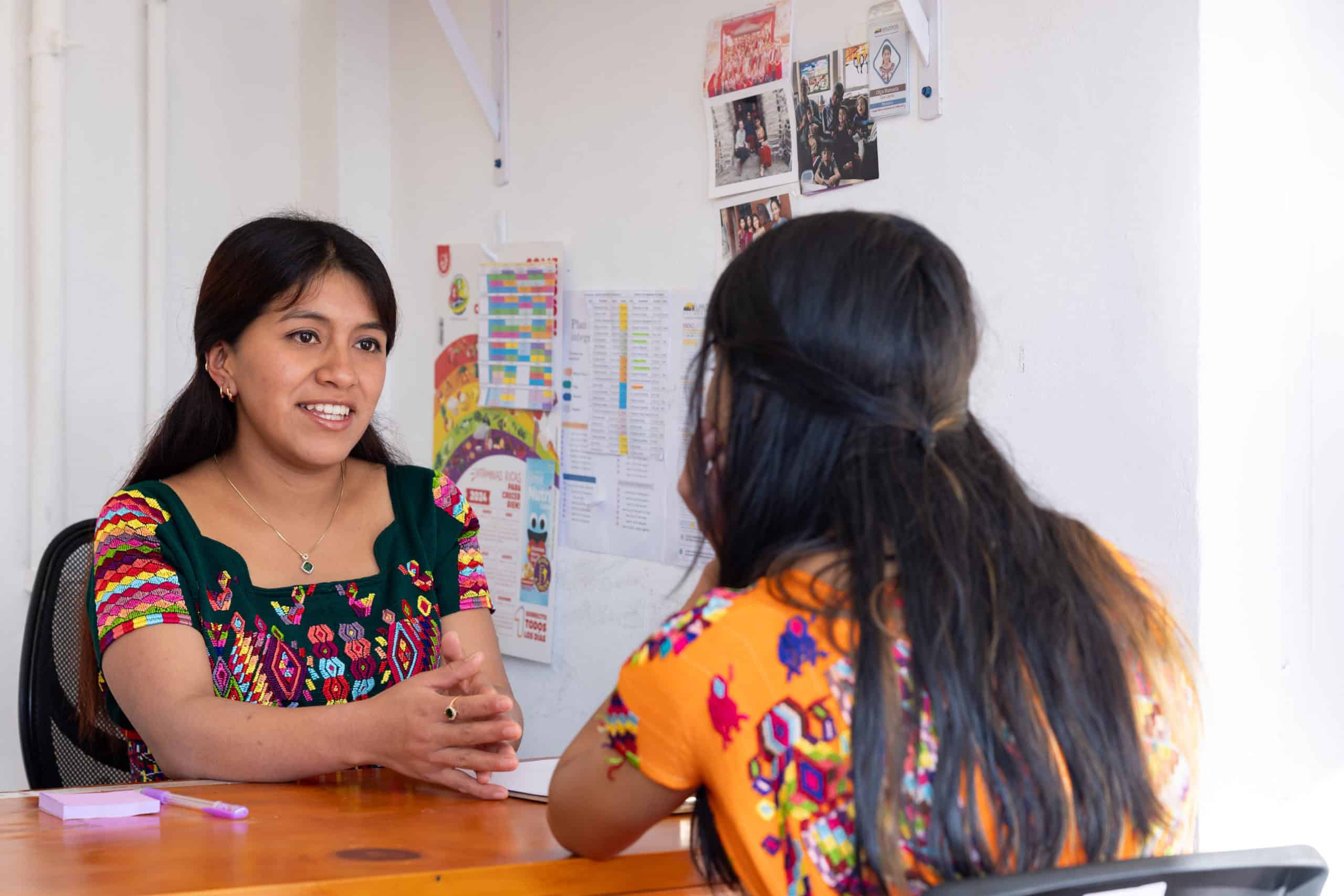 Two Ixil women engaged in a conversation at Colegio Horizontes, promoting education and community de.