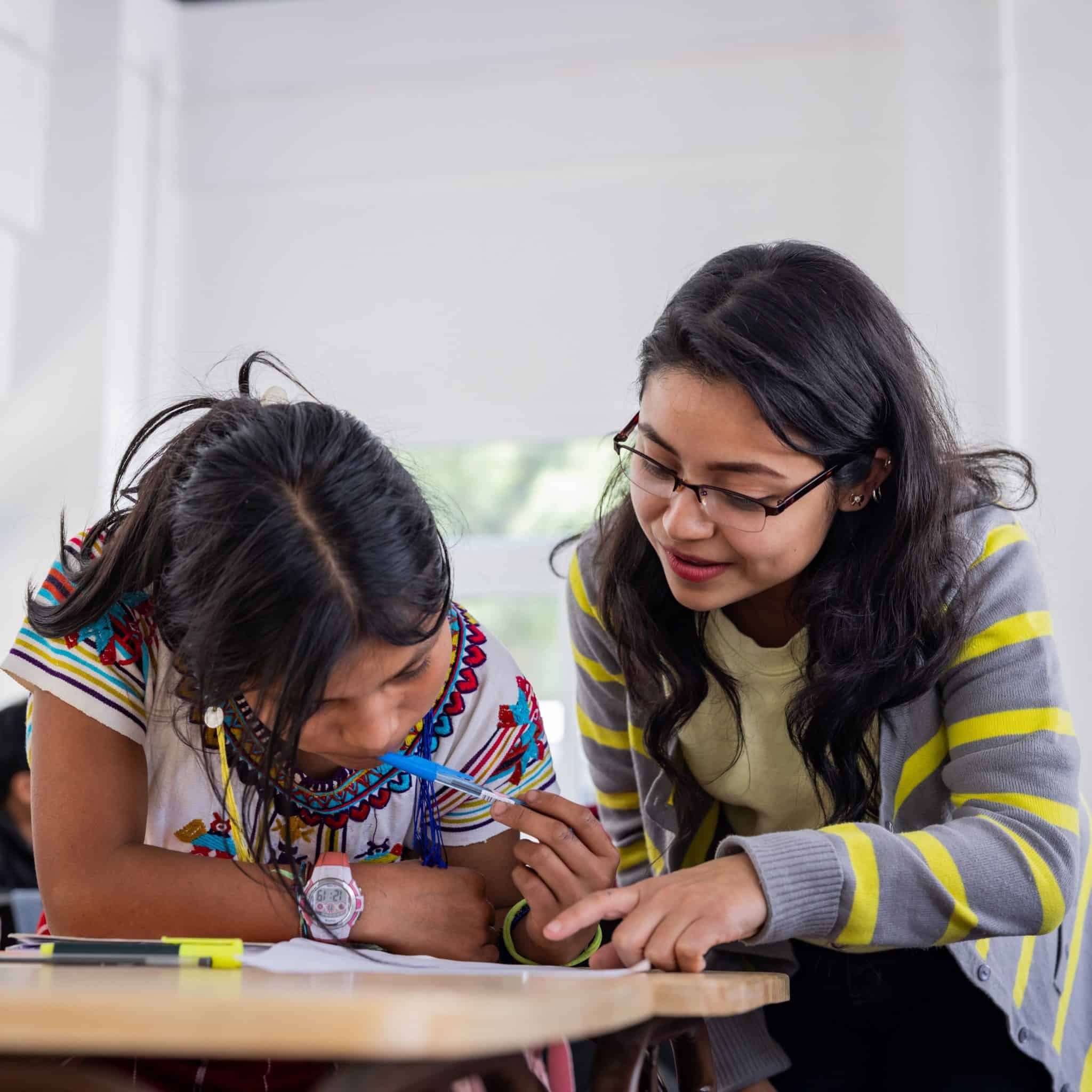 Woman helping a girl with schoolwork in a classroom setting.