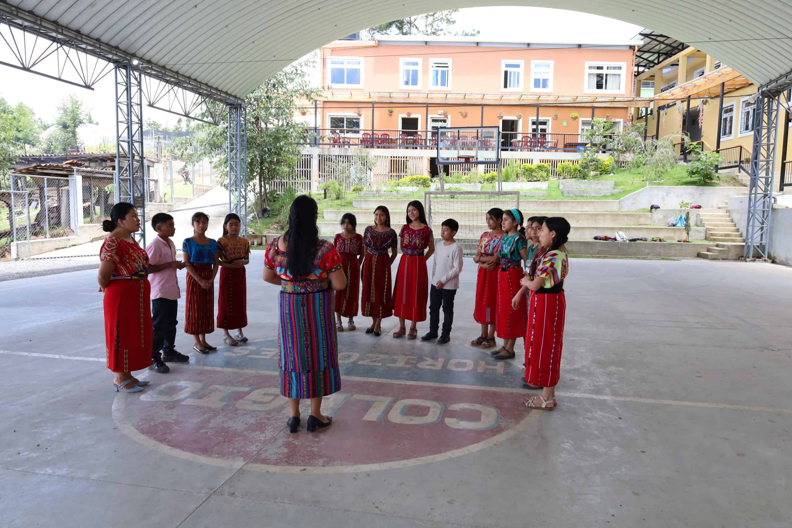 Students practicing traditional Ixil dance under a covered outdoor area.