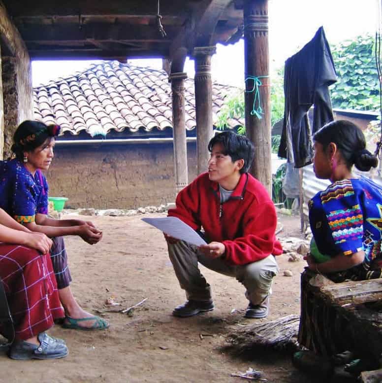 Volunteer engaging with Ixil community members in a traditional outdoor setting.