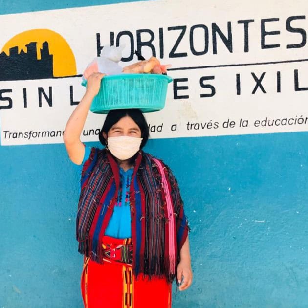 Woman with traditional clothing and face mask holding a basket in front of Limitless Horizons Ixil s.