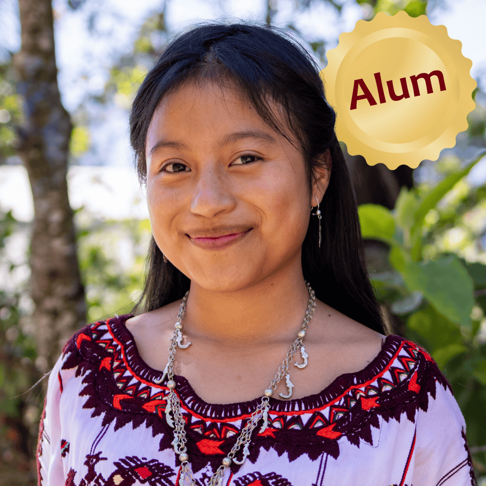 Young Ixil girl smiling outdoors, wearing traditional clothing.