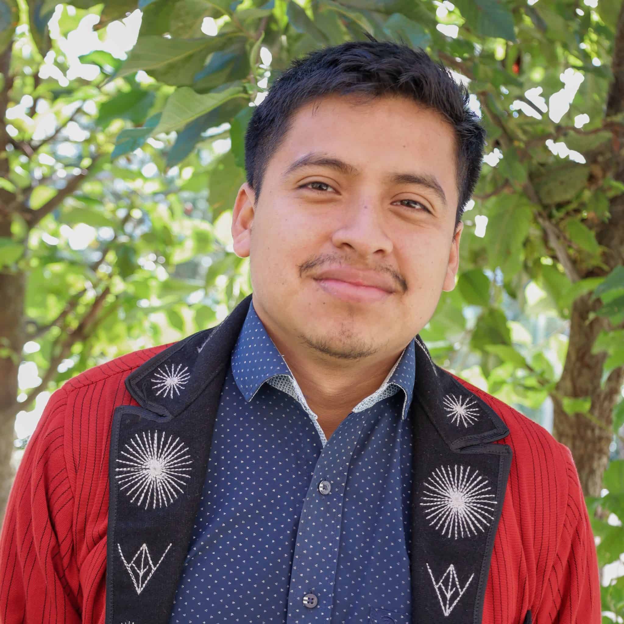 Young man smiling outdoors with green foliage background.